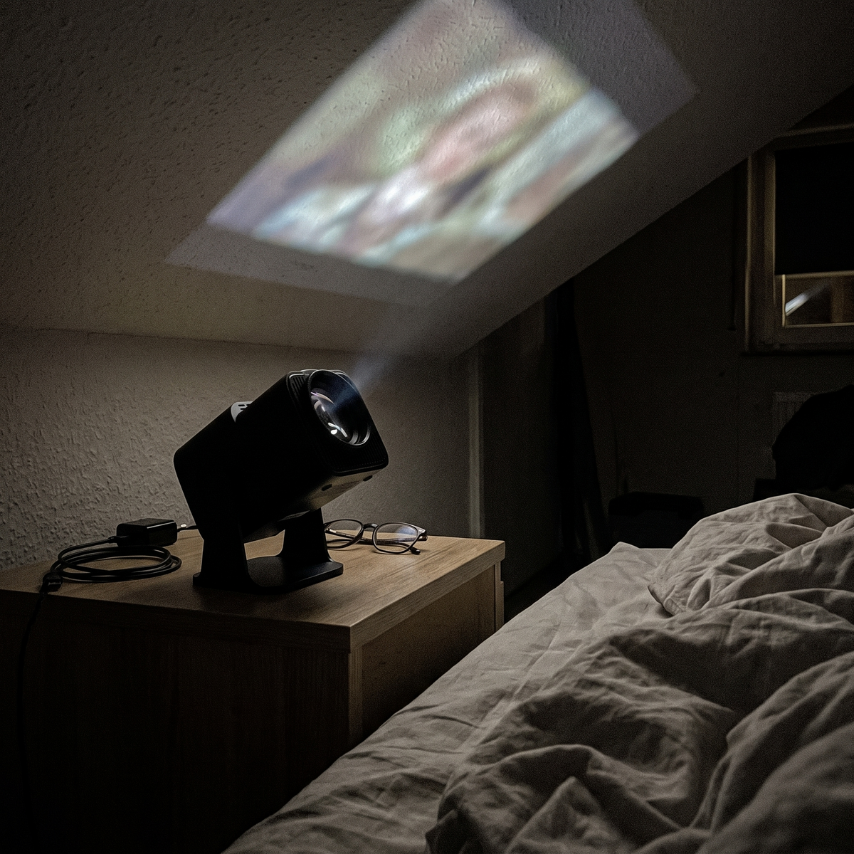 Mini projector on a nightstand tilted up to project onto the bedroom ceiling