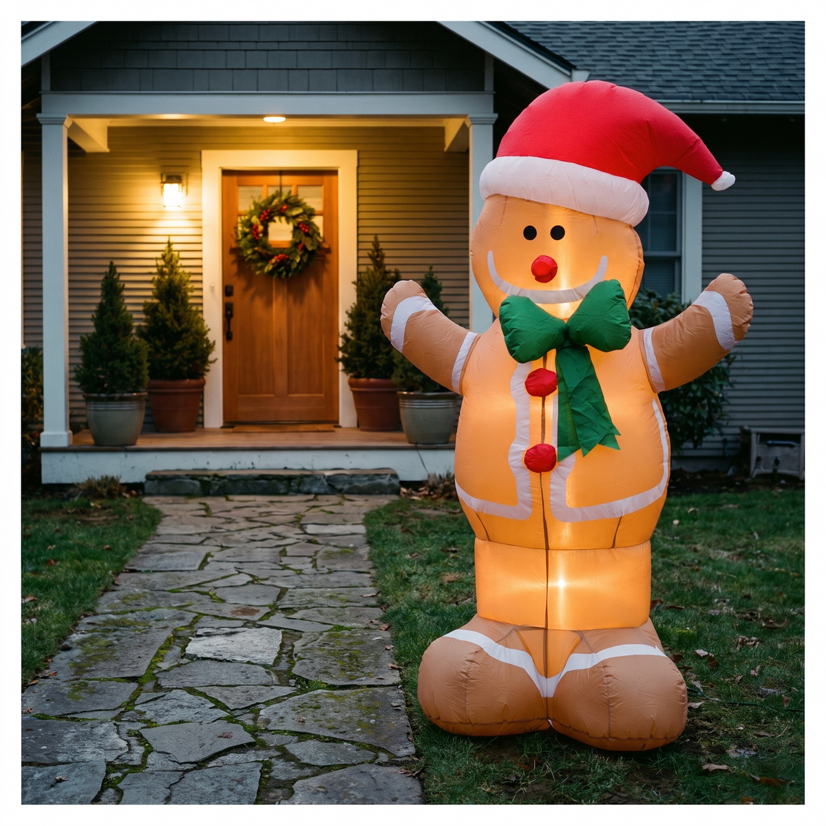 Inflatable gingerbread man beside a garden path and lit front porch at dusk