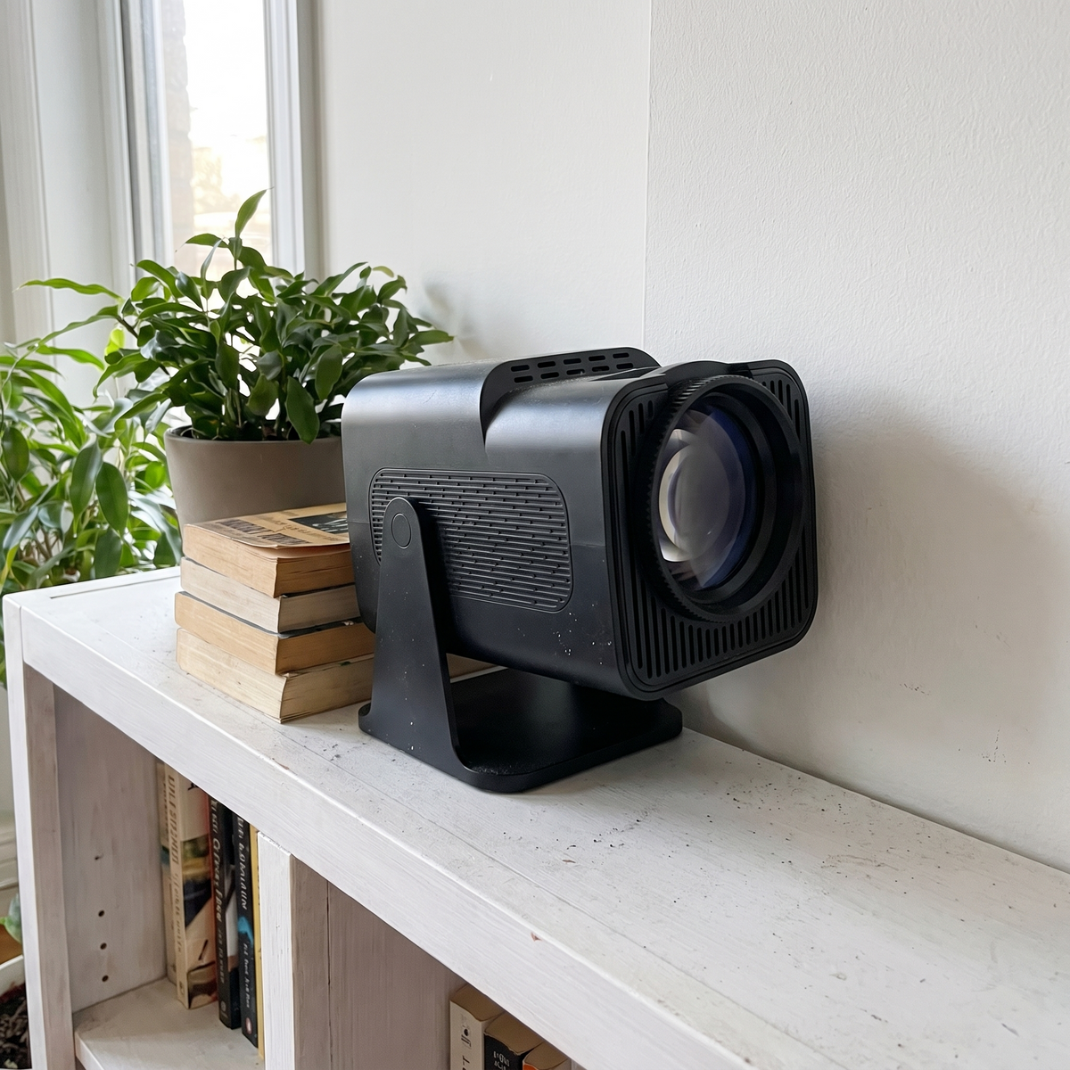 Mini projector on a bookshelf with its turret head angled toward the wall