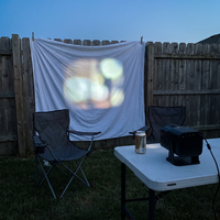 Mini projector projecting onto a bedsheet on a backyard fence at dusk