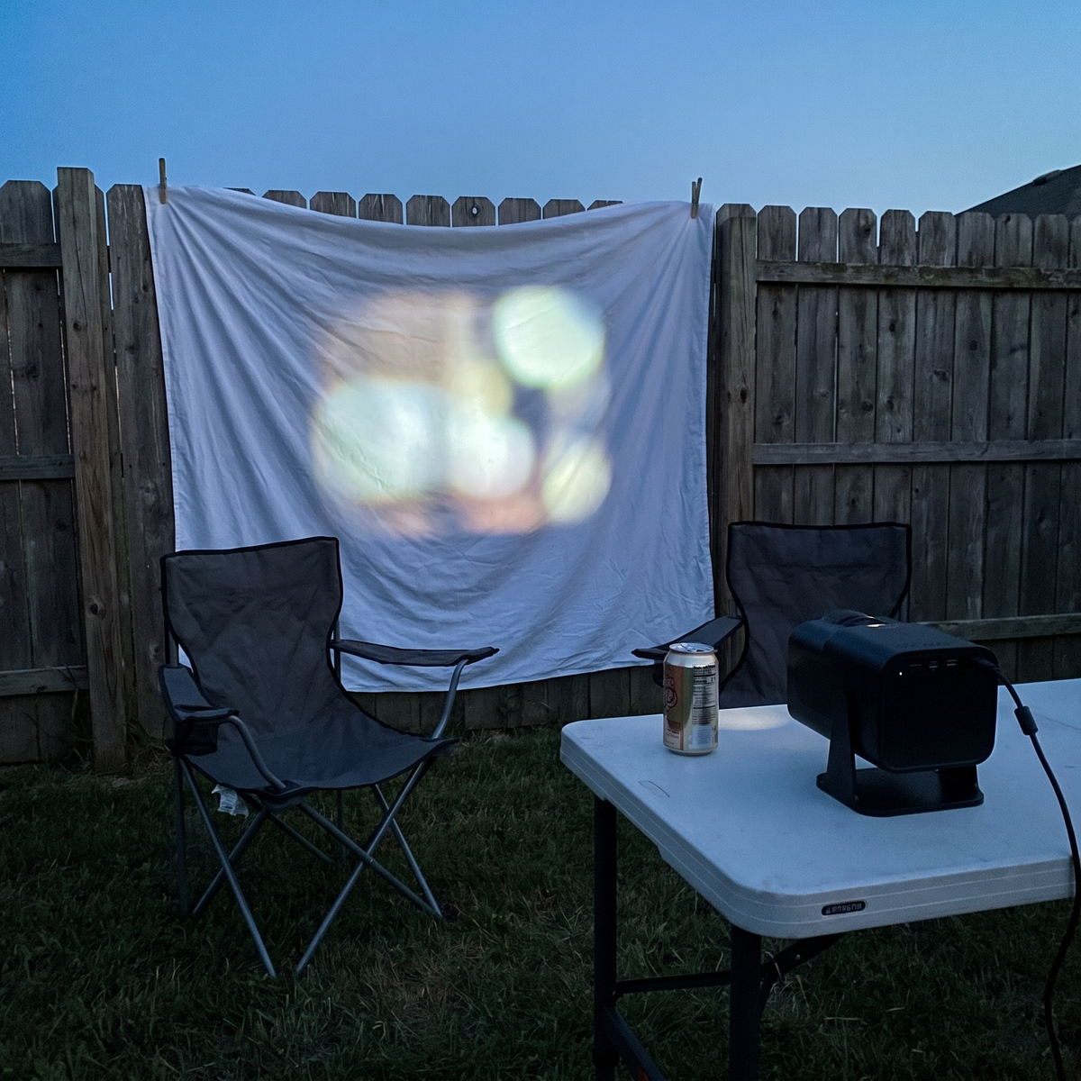 Mini projector projecting onto a bedsheet on a backyard fence at dusk