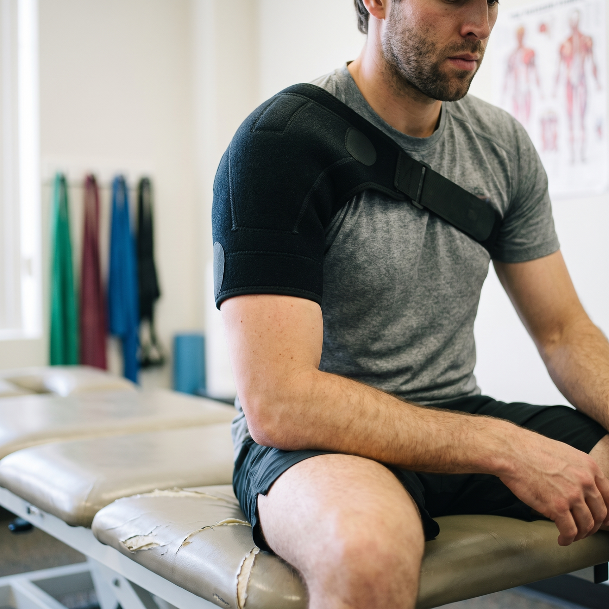 Man on a physiotherapy treatment bench wearing the black shoulder brace