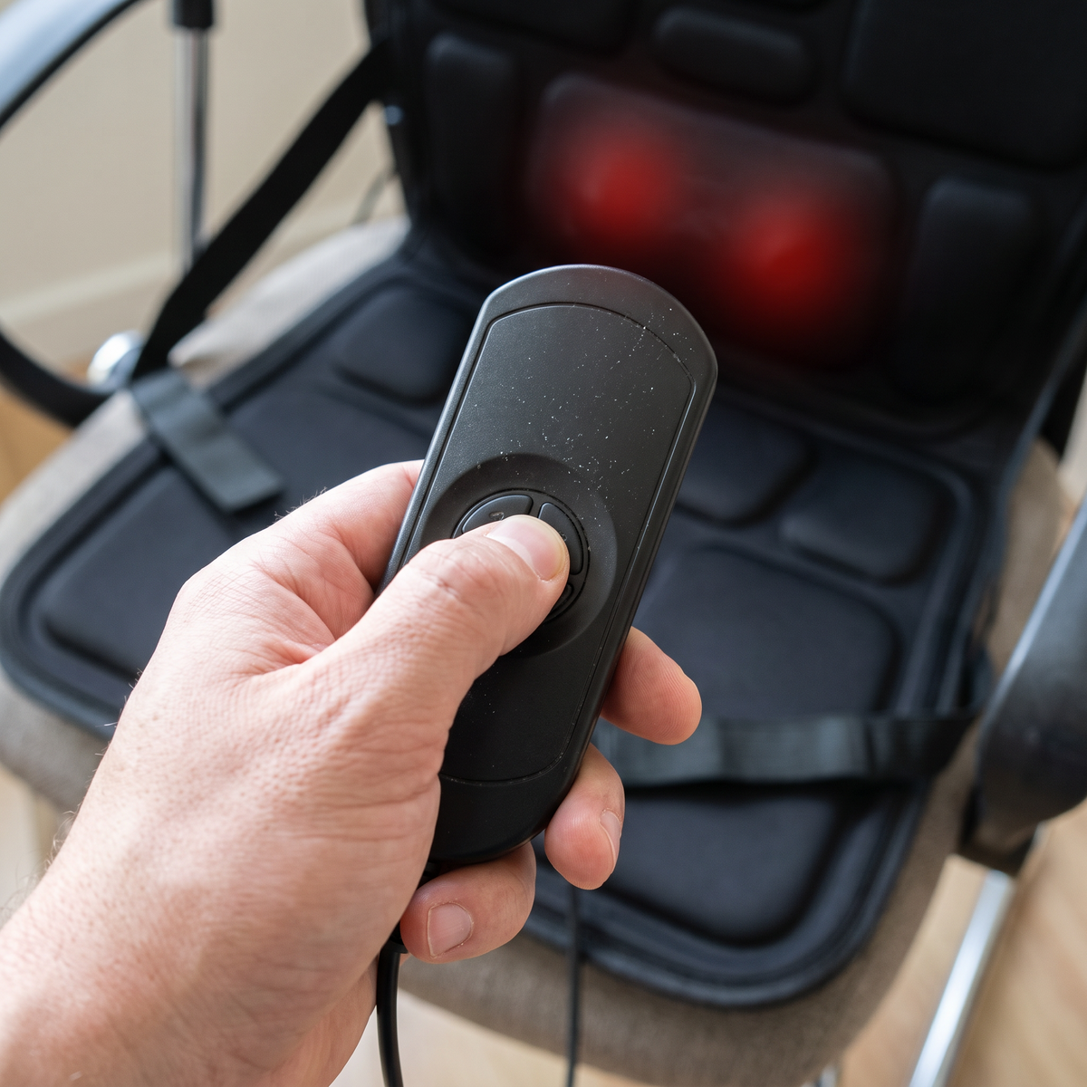 Hand pressing a button on the massage cushion's wired controller