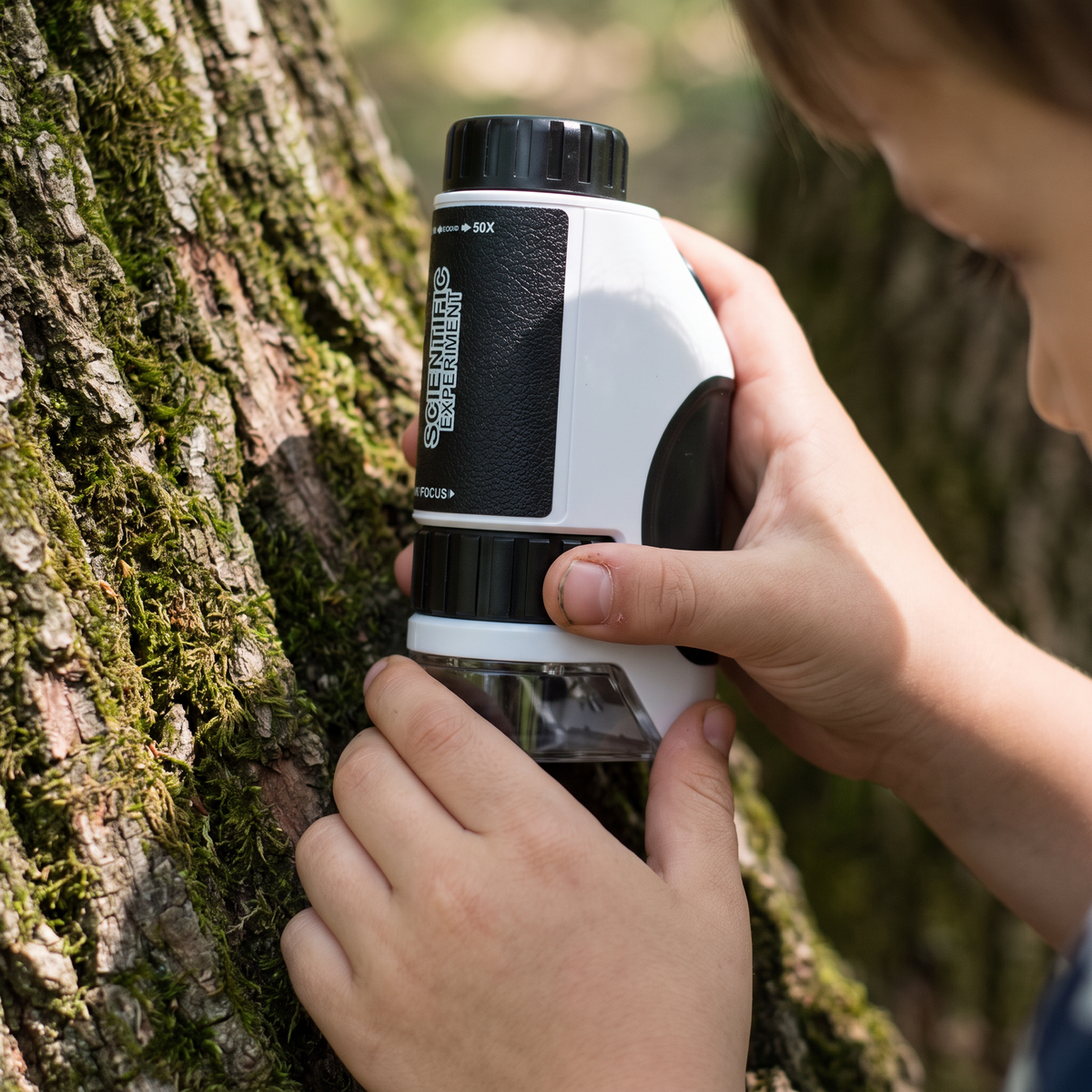 Hands turning the focus wheel of the handheld microscope against tree bark